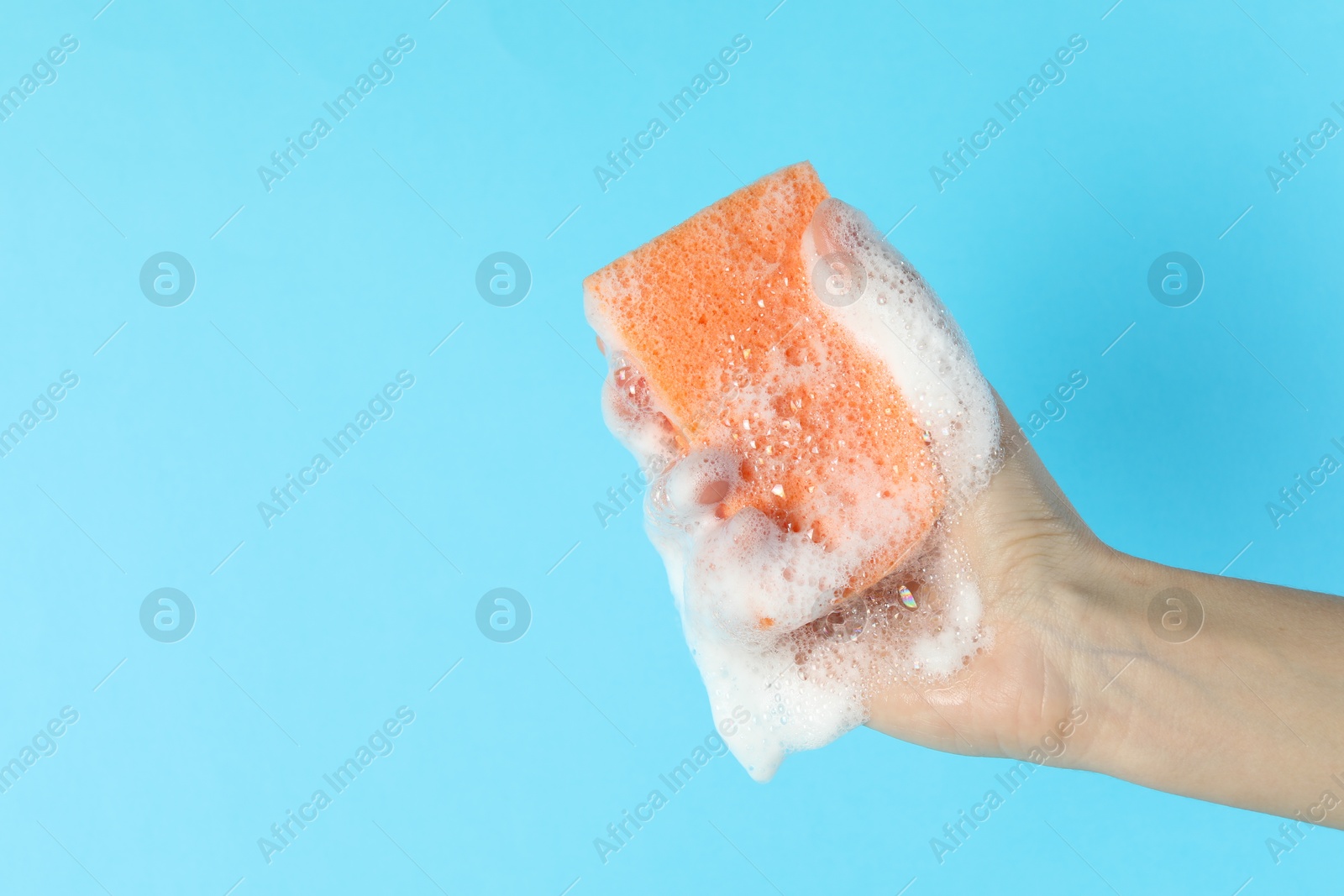 Photo of Woman holding sponge with foam on light blue background, closeup. Space for text