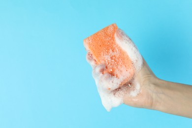 Photo of Woman holding sponge with foam on light blue background, closeup. Space for text