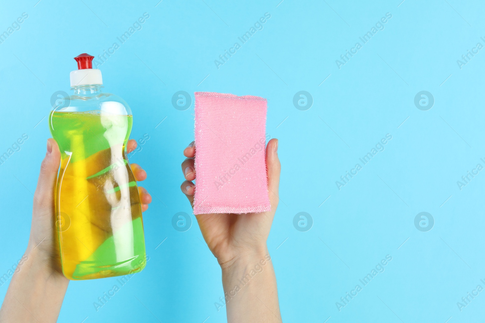 Photo of Woman holding sponge and bottle with detergent on light blue background, closeup. Space for text