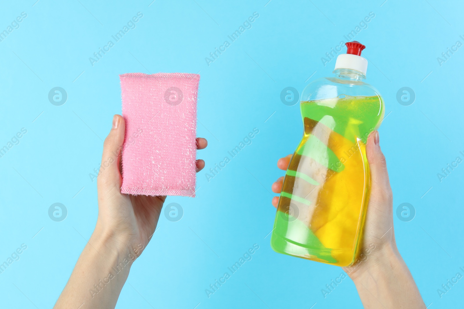 Photo of Woman holding sponge and bottle with detergent on light blue background, closeup