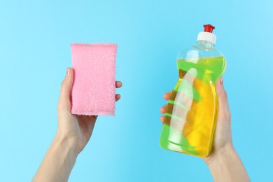 Photo of Woman holding sponge and bottle with detergent on light blue background, closeup