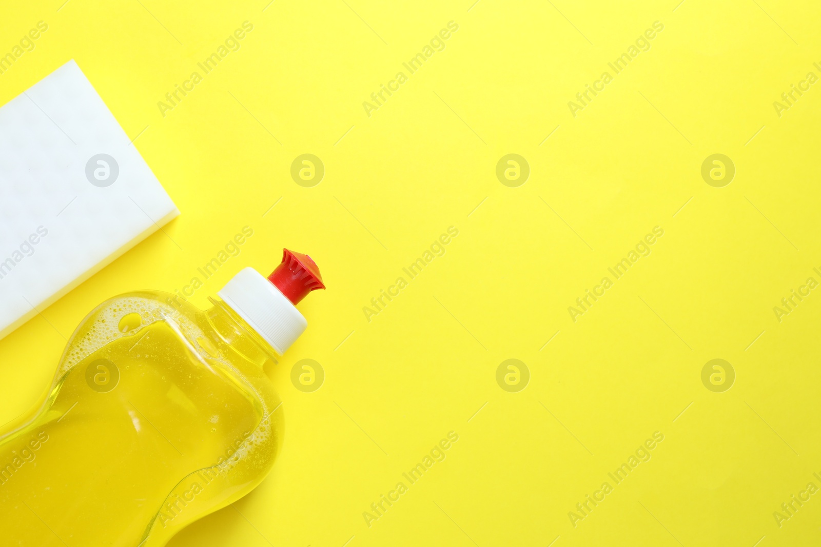 Photo of Sponge and bottle with detergent on yellow background, top view. Space for text