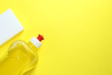 Photo of Sponge and bottle with detergent on yellow background, top view. Space for text