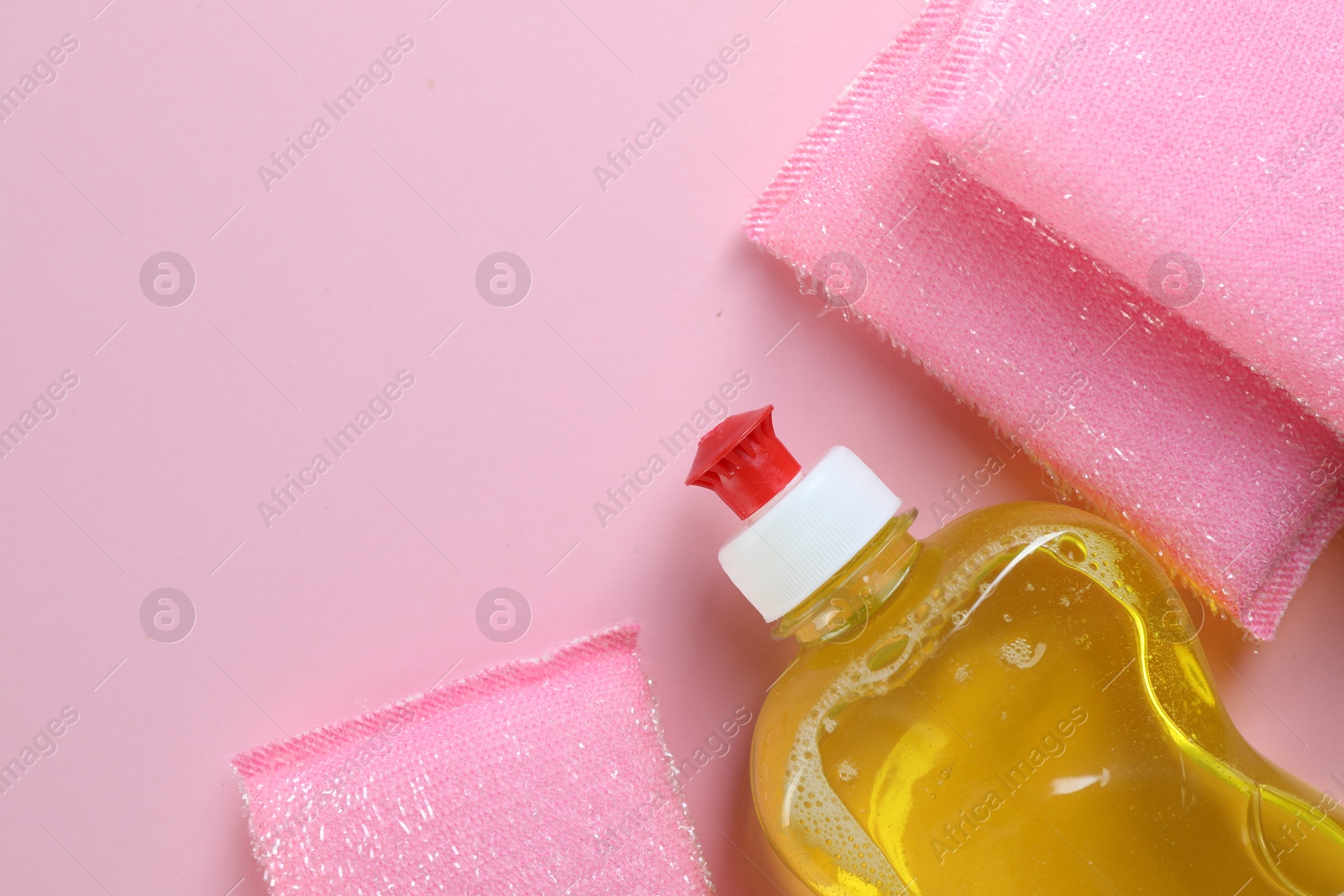 Photo of Sponges and bottle with detergent on pink background, flat lay. Space for text