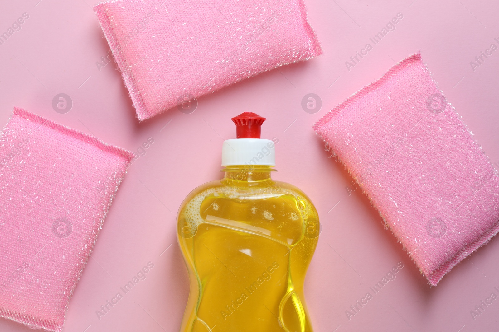 Photo of Sponges and bottle with detergent on pink background, flat lay