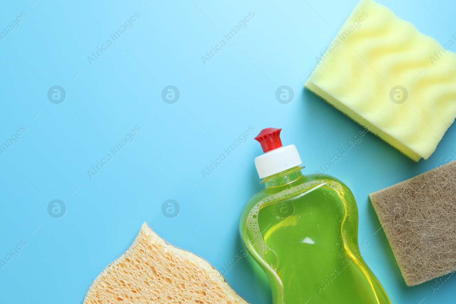 Photo of Different sponges and bottle with detergent on light blue background, flat lay. Space for text