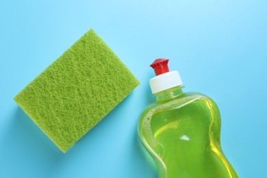 Photo of Sponge and bottle with detergent on light blue background, flat lay