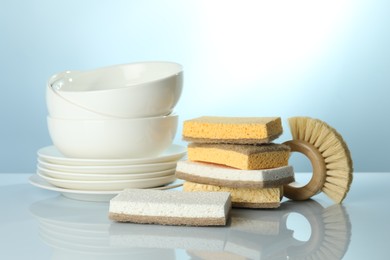 Photo of Stack of sponges, brush and dishware on light table, closeup