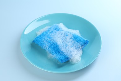 Photo of One sponge with foam and plate on light blue background, closeup