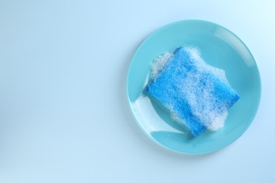 Photo of One sponge with foam and plate on light blue background, top view. Space for text