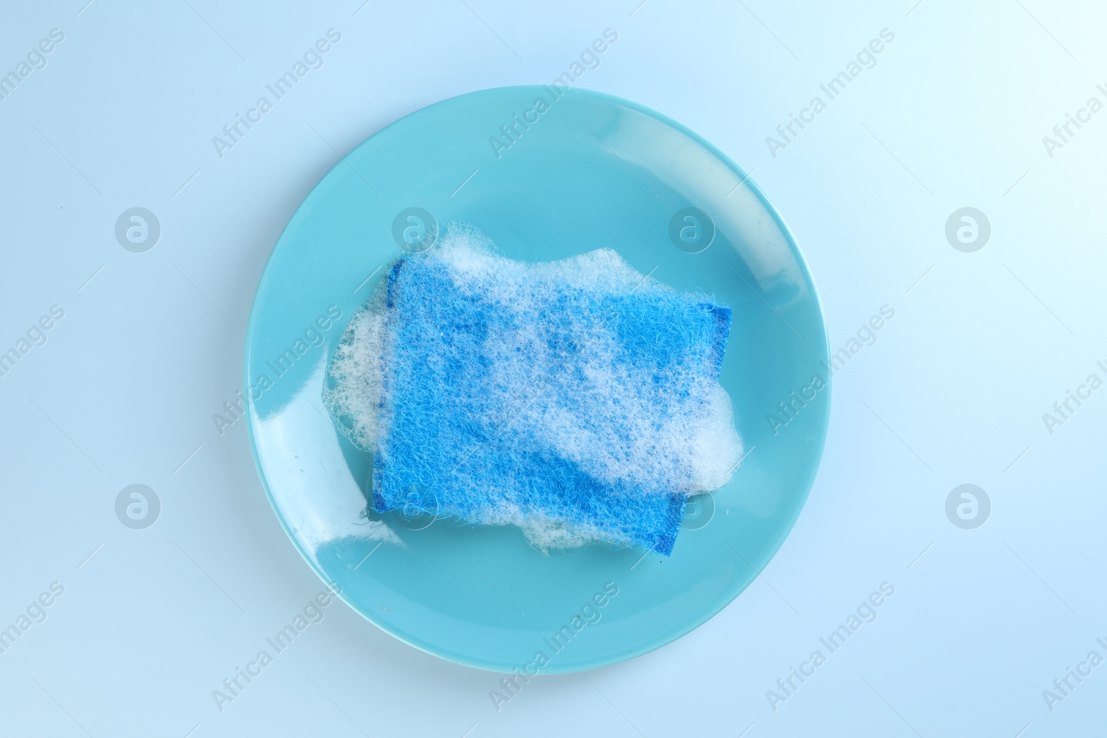 Photo of One sponge with foam and plate on light blue background, top view