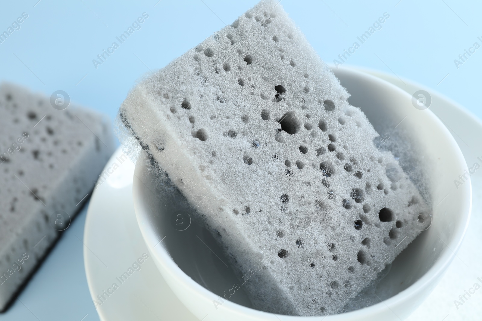 Photo of Sponge with foam and dishware on light blue background, closeup