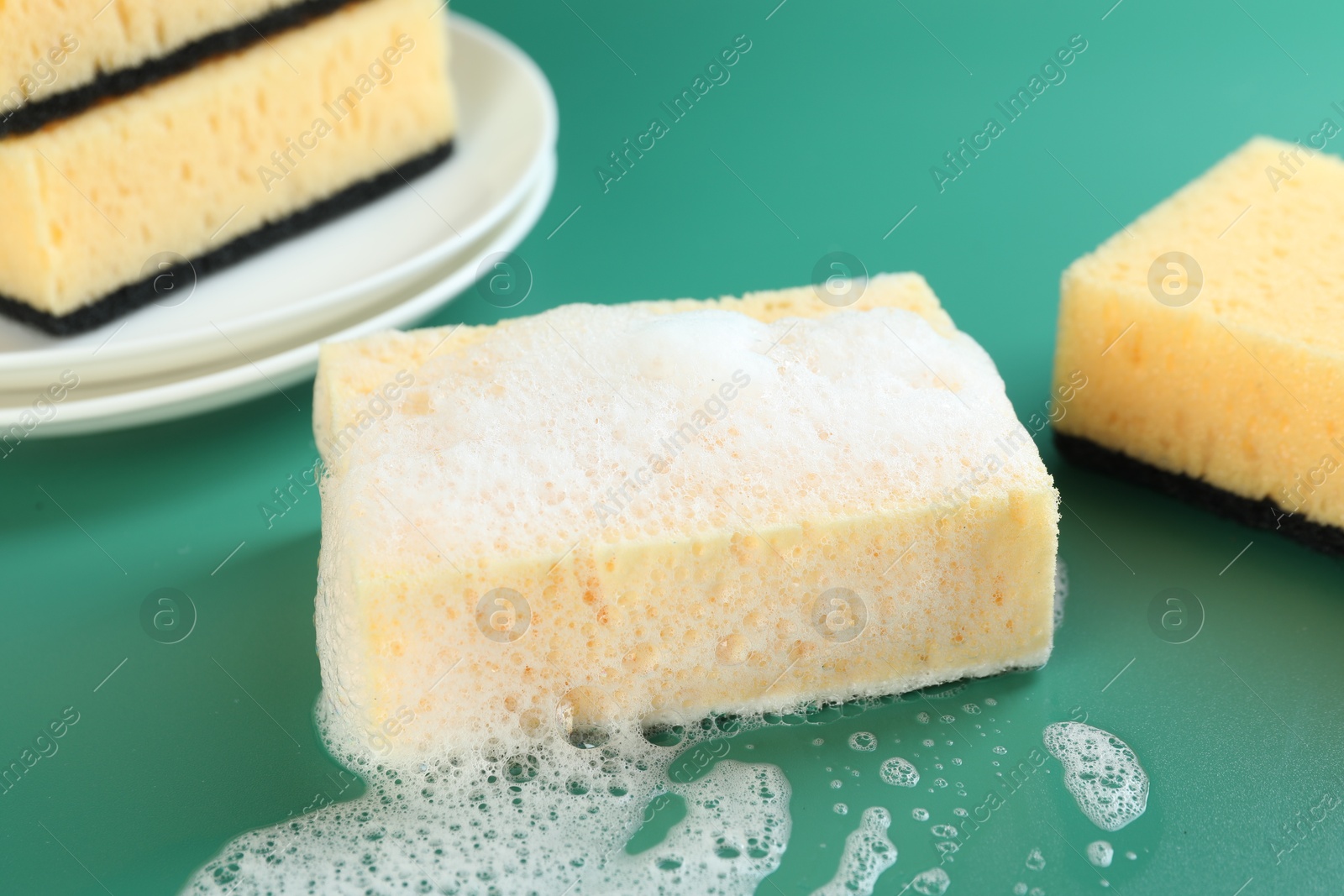 Photo of Sponge with foam among ones on green background, closeup