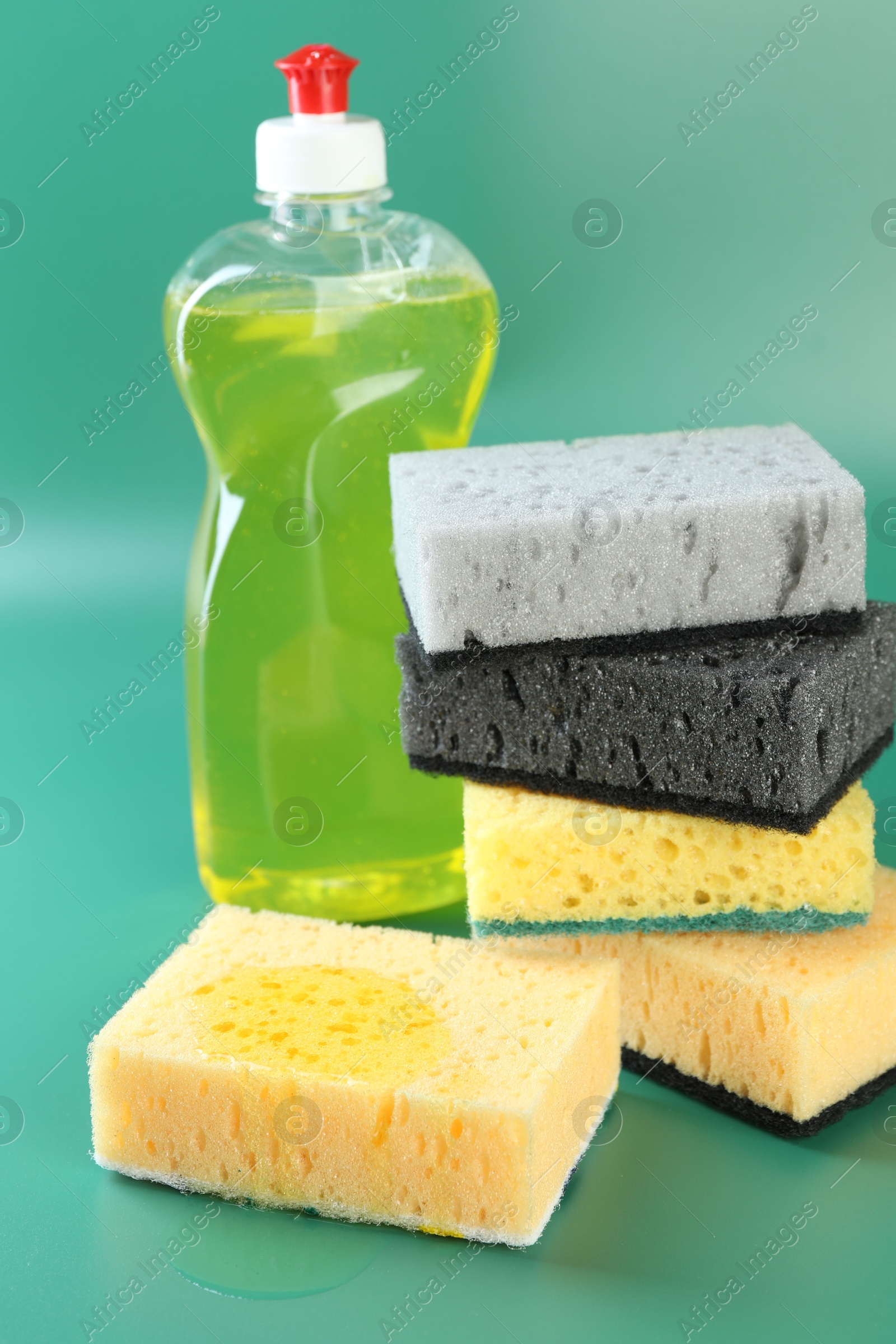 Photo of Sponge with detergent and stack of ones on green background, closeup