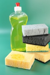 Photo of Sponge with detergent and stack of ones on green background, closeup