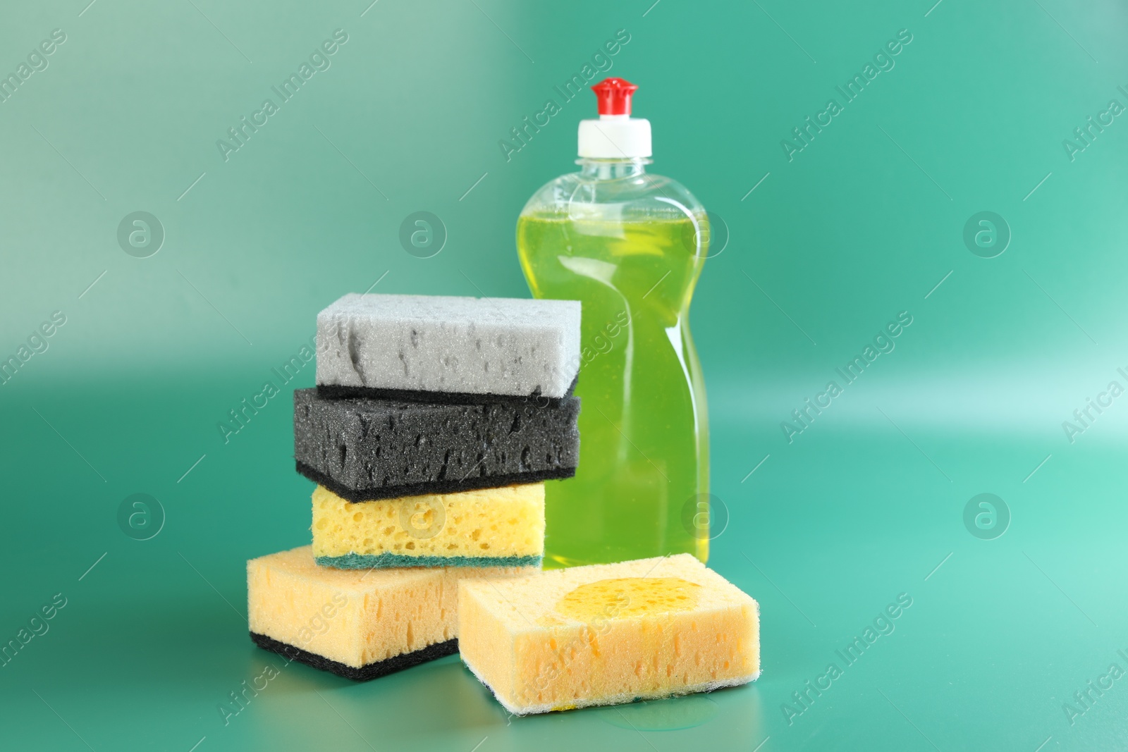 Photo of Sponge with detergent and stack of ones on green background, closeup