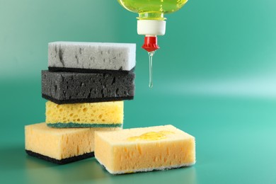 Photo of Pouring detergent from bottle onto sponge on green background, closeup