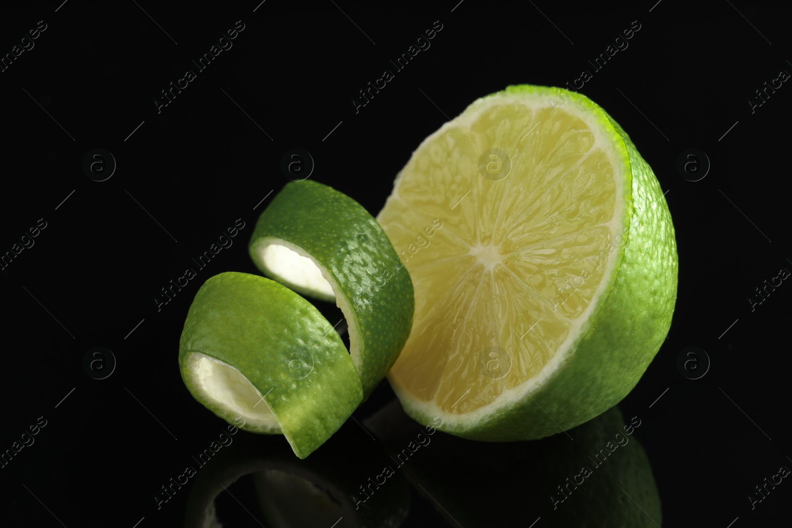 Photo of Lime peel and half of fresh fruit on black mirror surface, closeup