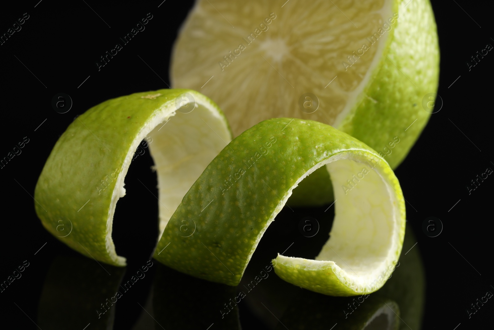 Photo of Lime peel and half of fresh fruit on black mirror surface, closeup