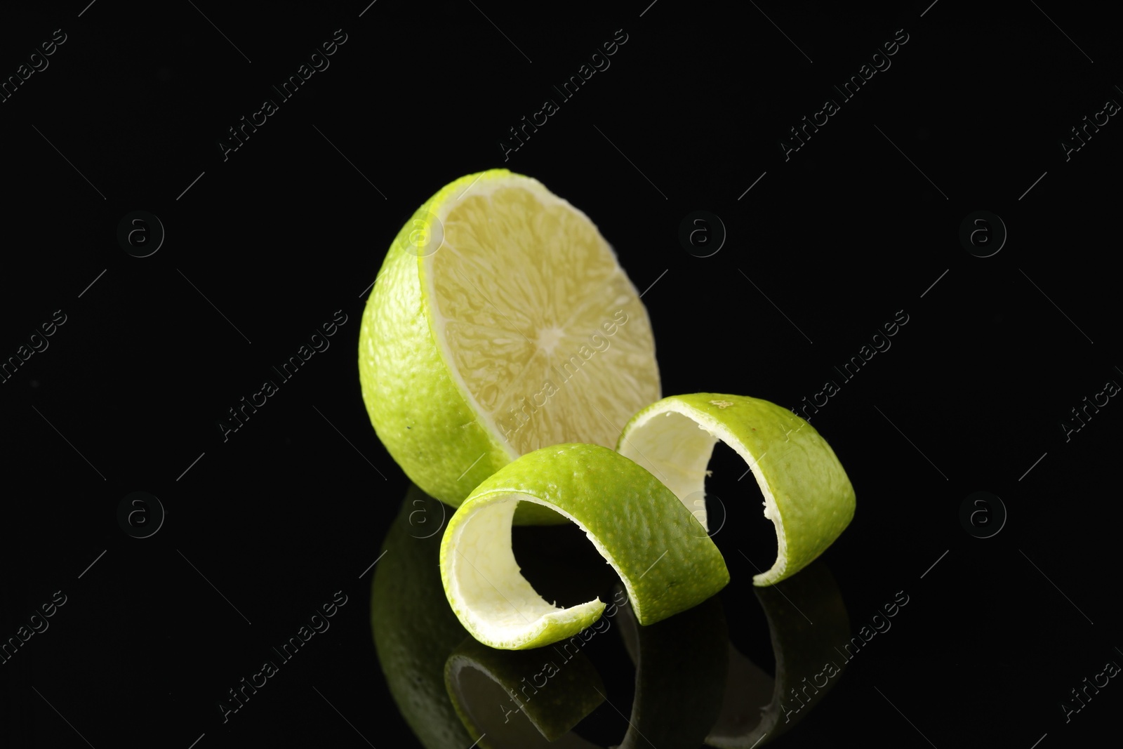 Photo of Lime peel and half of fresh fruit on black mirror surface, closeup