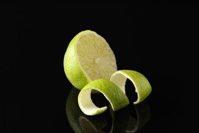 Photo of Lime peel and half of fresh fruit on black mirror surface, closeup