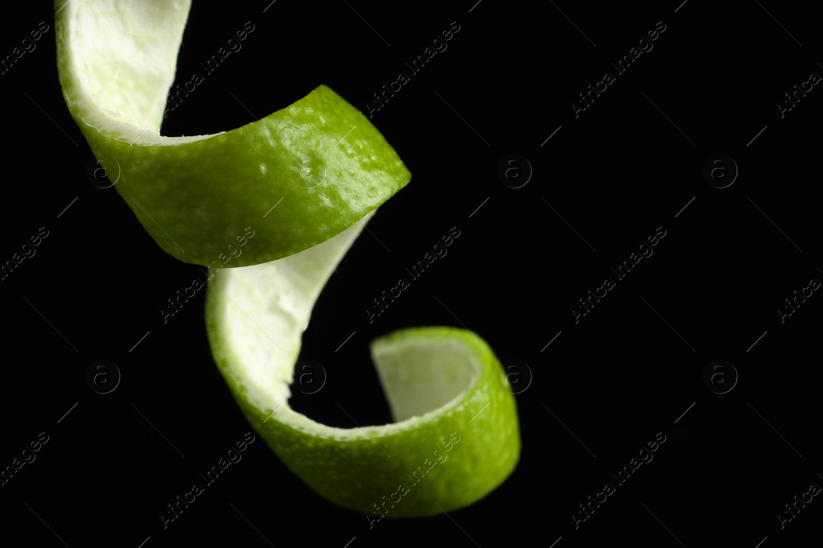 Photo of One curly lime peel on black background, closeup. Space for text