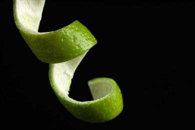 Photo of One curly lime peel on black background, closeup. Space for text