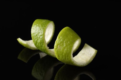 Photo of One curly lime peel on black mirror surface, closeup