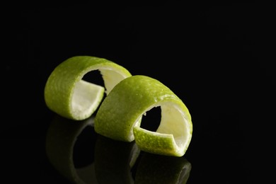 Photo of One curly lime peel on black mirror surface, closeup