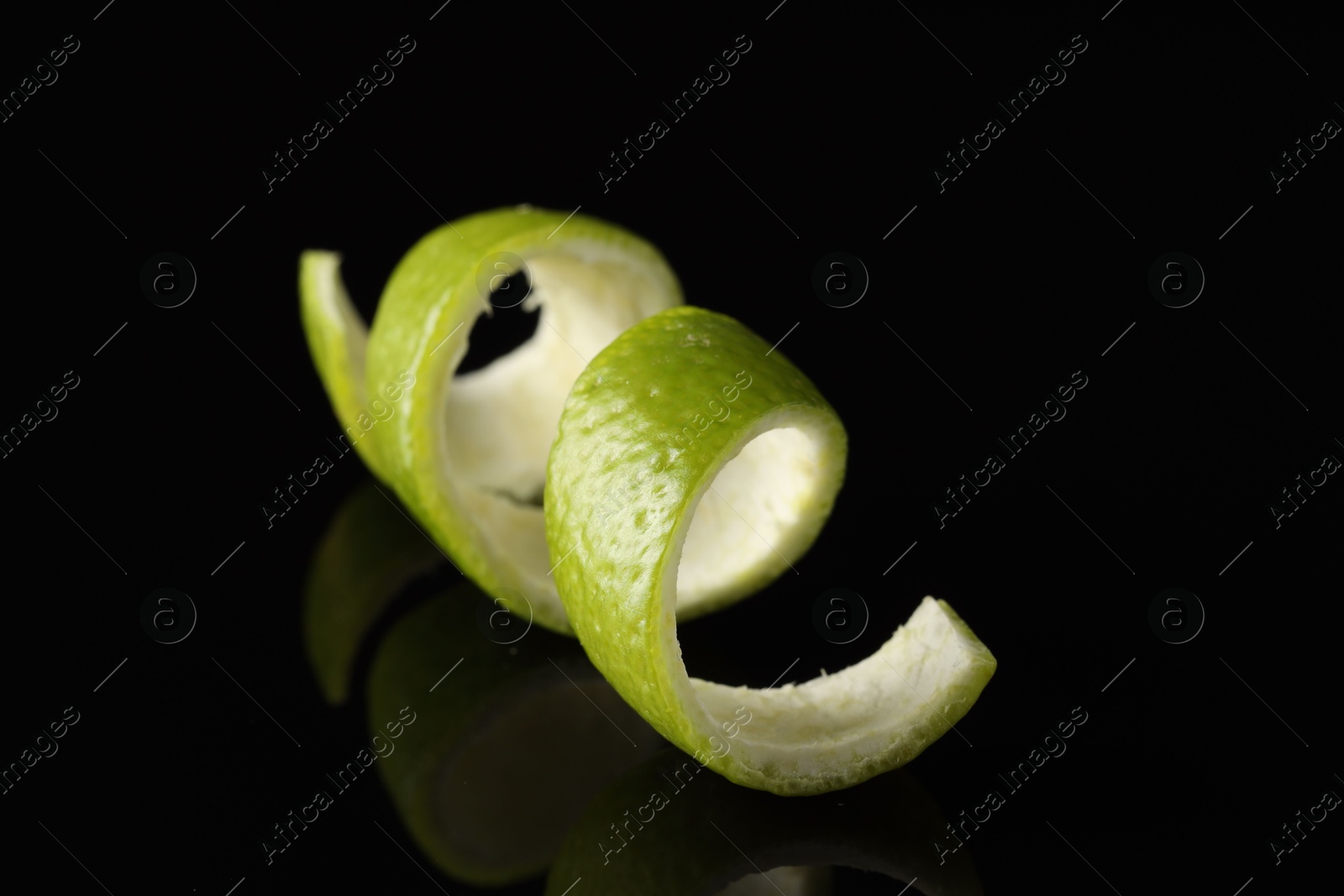 Photo of One curly lime peel on black mirror surface, closeup