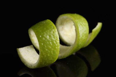 Photo of One curly lime peel on black mirror surface, closeup