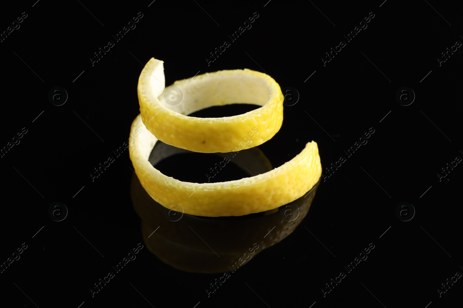 Photo of One curly lemon peel on black mirror surface, closeup