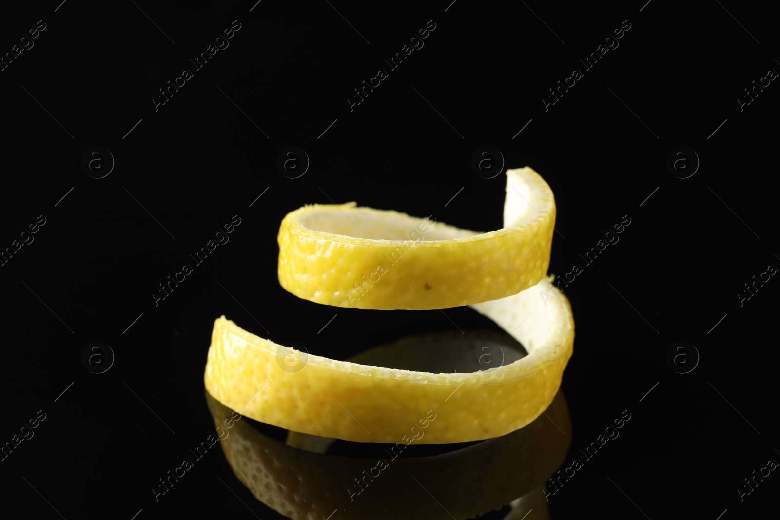 Photo of One curly lemon peel on black mirror surface, closeup