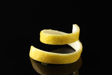 Photo of One curly lemon peel on black mirror surface, closeup