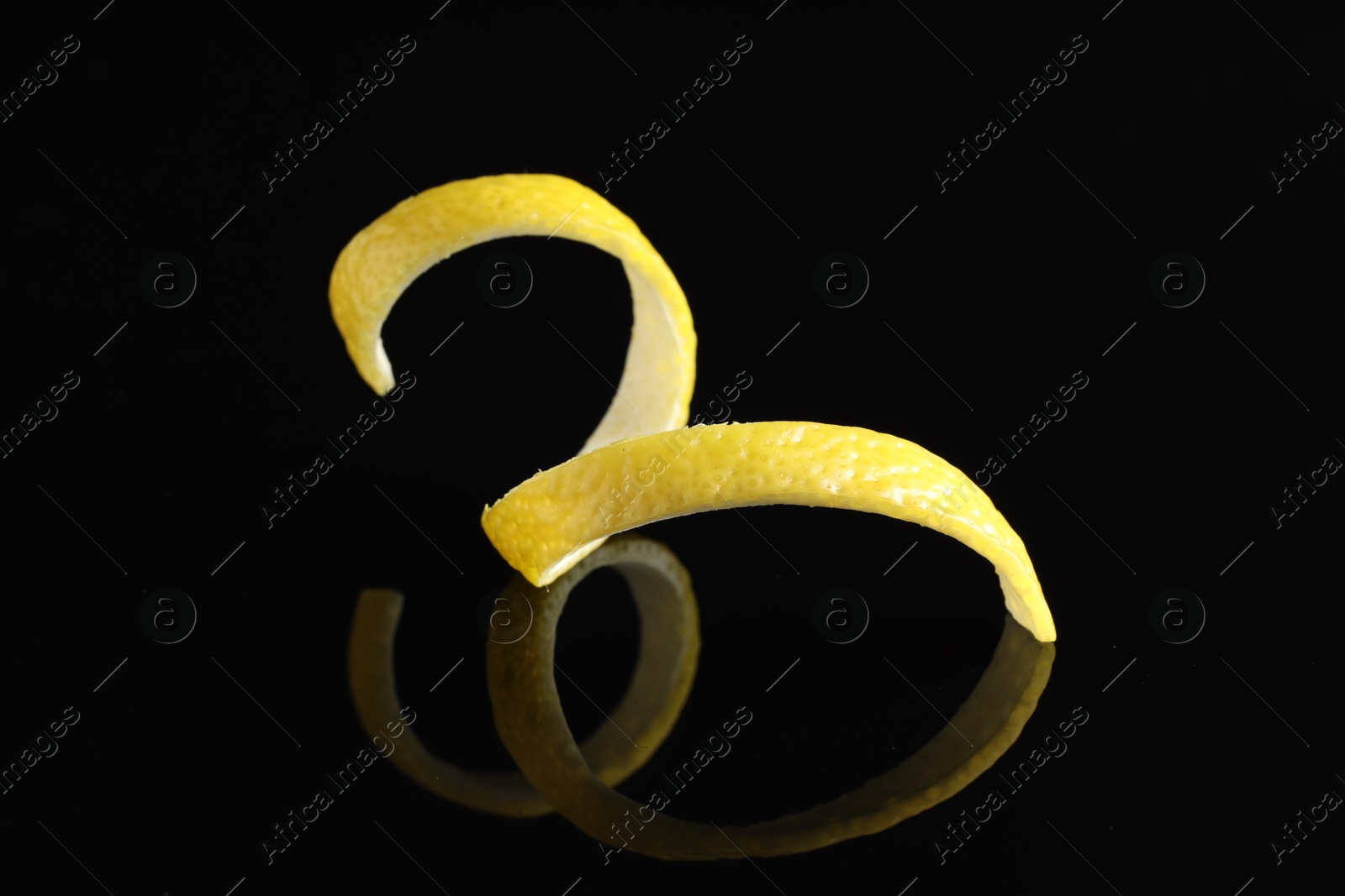 Photo of One curly lemon peel on black mirror surface, closeup