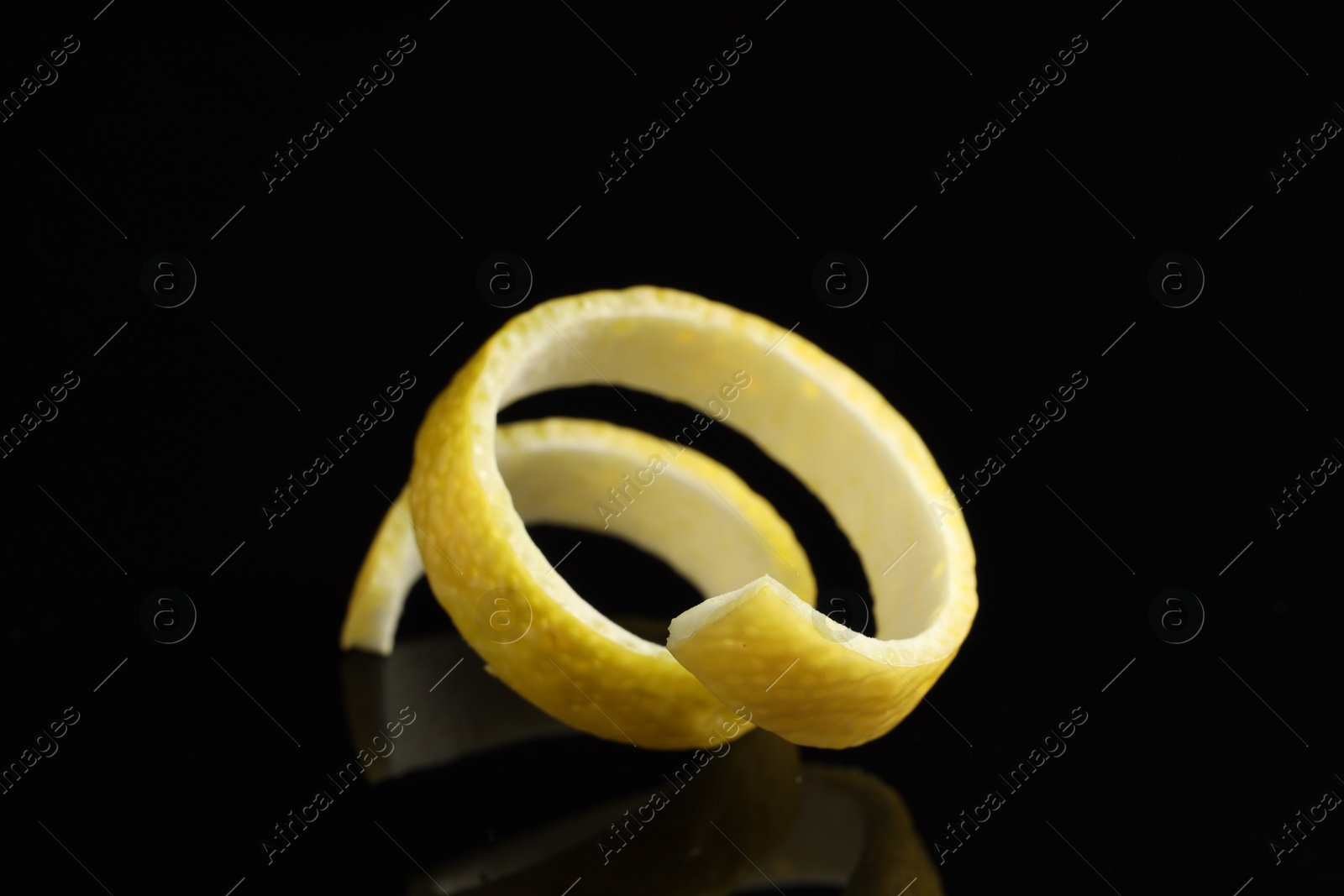 Photo of One curly lemon peel on black mirror surface, closeup