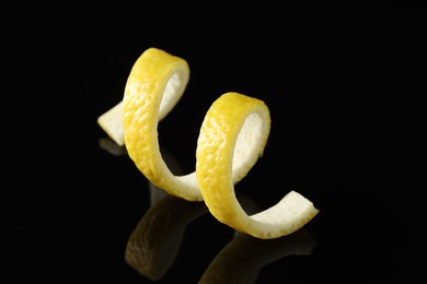 Photo of One curly lemon peel on black mirror surface, closeup