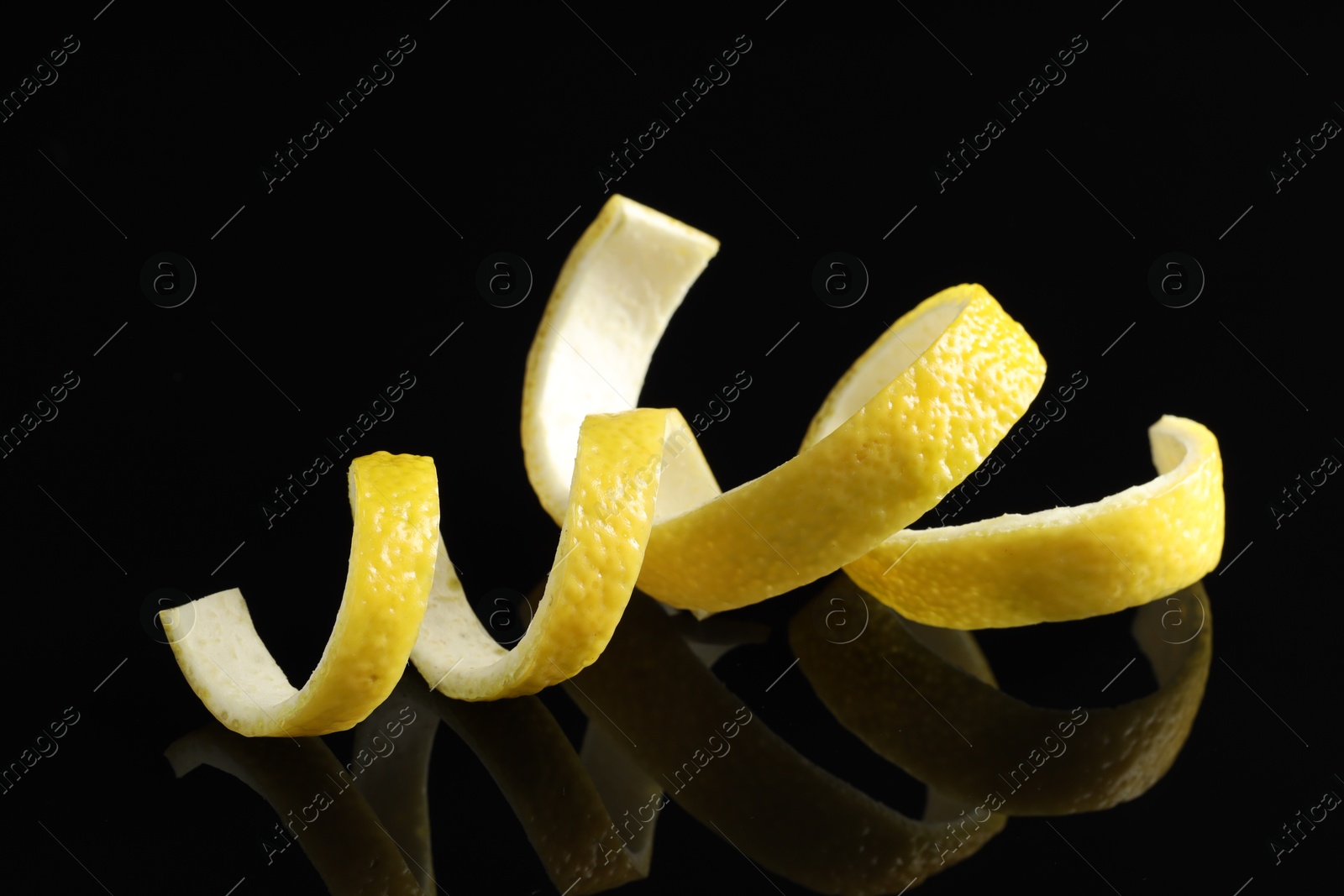 Photo of Curly lemon peels on black background, closeup