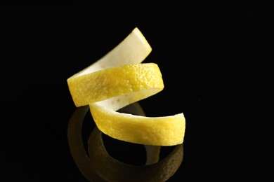 Photo of One curly lemon peel on black mirror surface, closeup