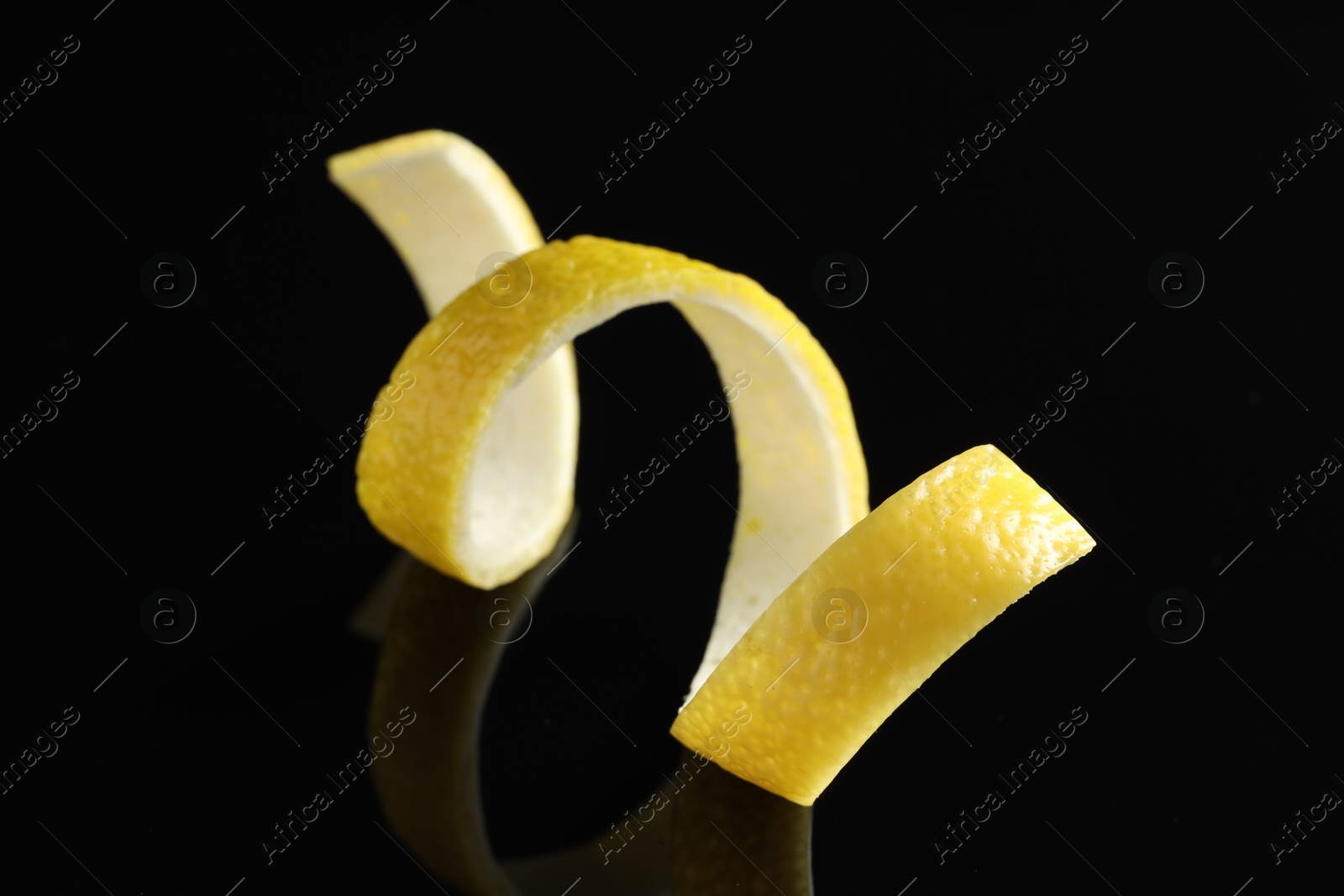 Photo of One curly lemon peel on black mirror surface, closeup