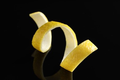 Photo of One curly lemon peel on black mirror surface, closeup