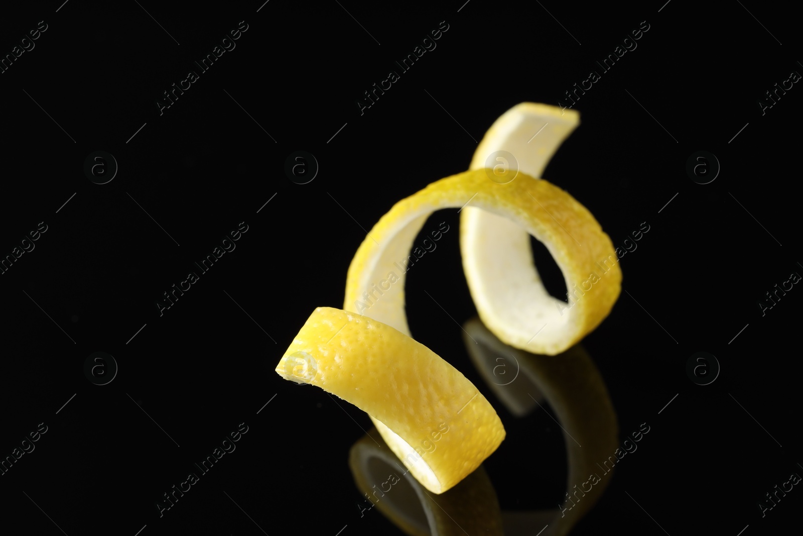 Photo of One curly lemon peel on black mirror surface, closeup