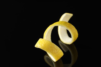 Photo of One curly lemon peel on black mirror surface, closeup