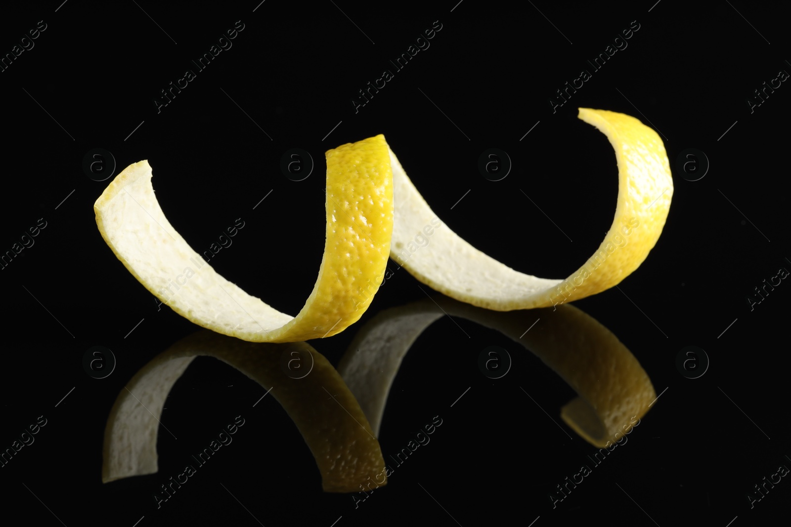 Photo of One curly lemon peel on black mirror surface, closeup