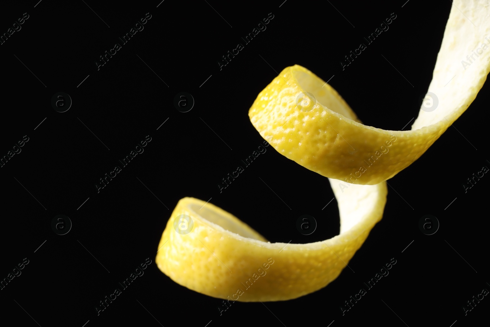 Photo of One curly lemon peel on black background, closeup. Space for text