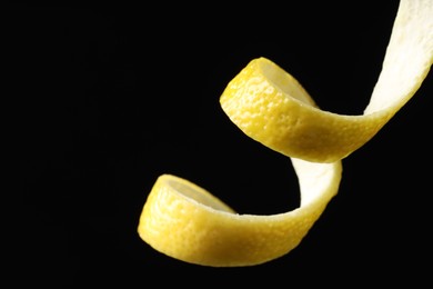 Photo of One curly lemon peel on black background, closeup. Space for text