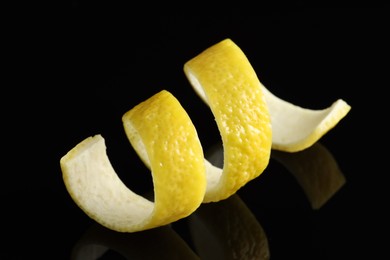 Photo of One curly lemon peel on black mirror surface, closeup