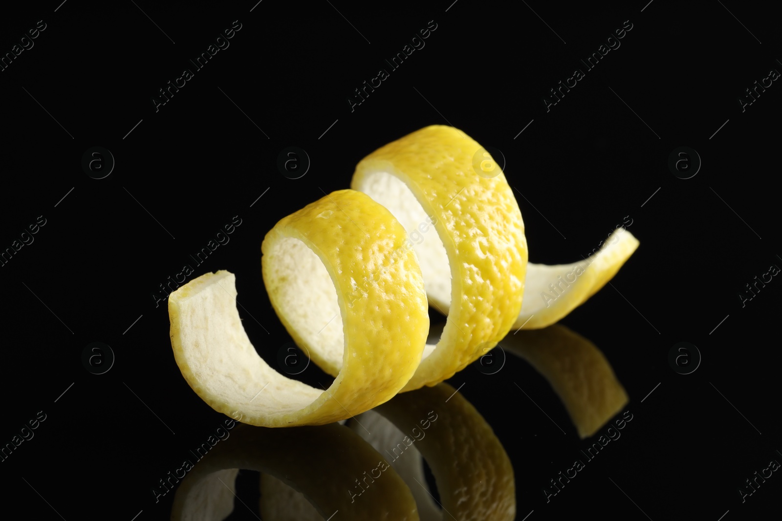 Photo of One curly lemon peel on black mirror surface, closeup