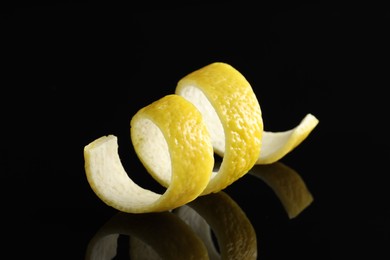 Photo of One curly lemon peel on black mirror surface, closeup