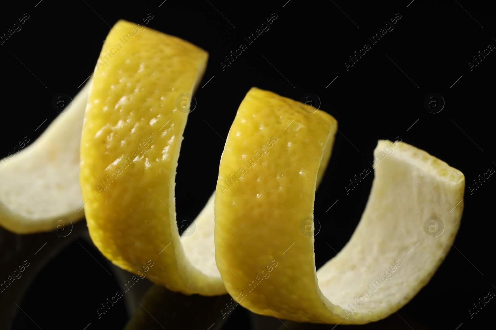 Photo of One curly lemon peel on black mirror surface, closeup